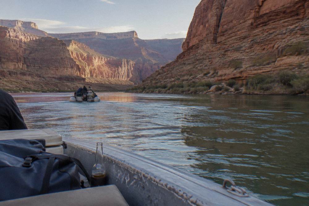 A motorized raft carrying passengers along a calm section of the Colorado River between canyon walls