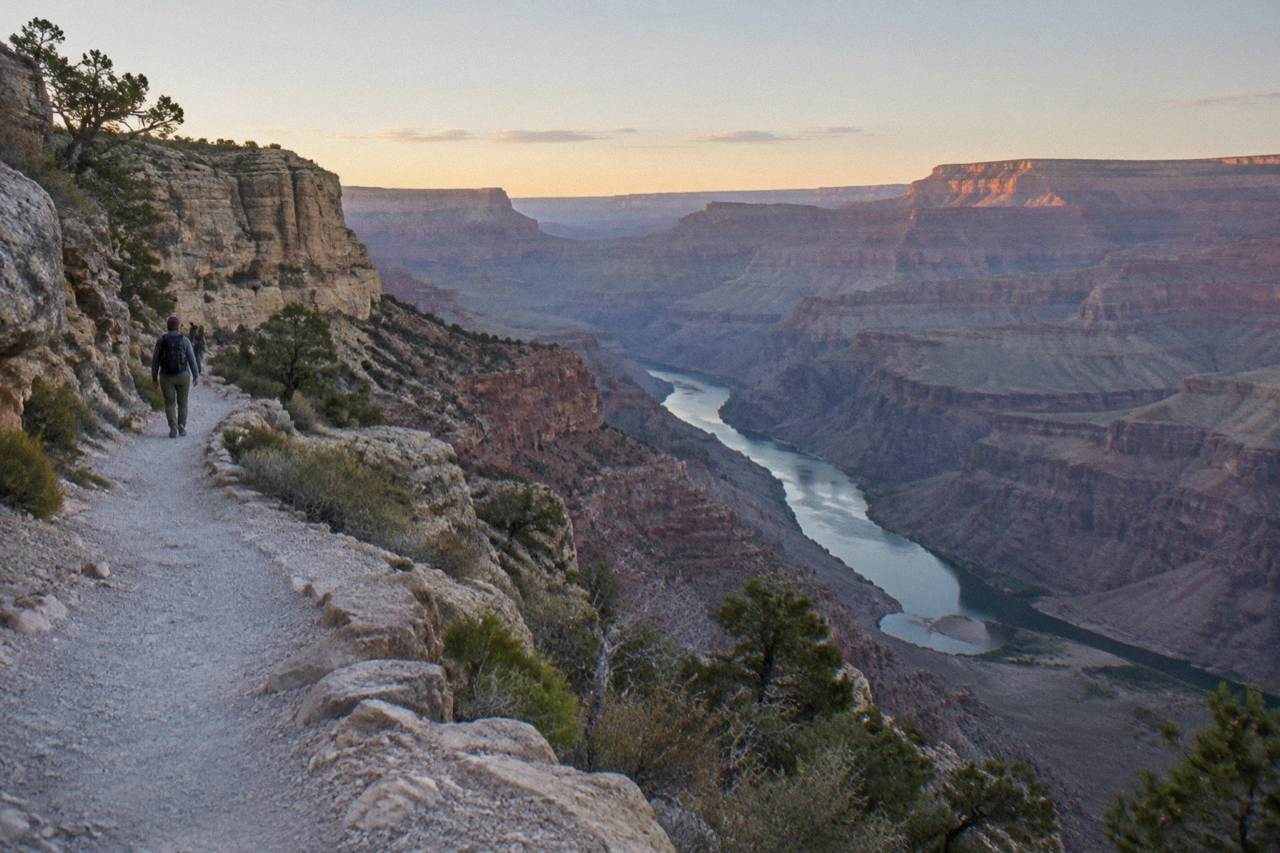 Layered rock walls of the Grand Canyon rising above the Colorado River in calm morning light