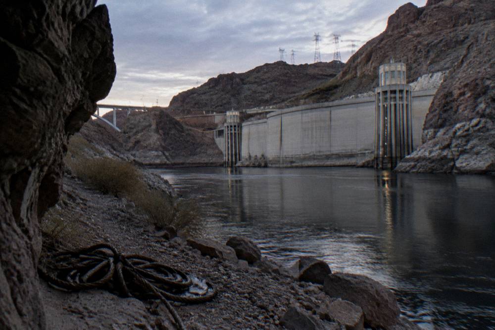 Smooth dark river water between rocky canyon walls near the base of a concrete dam.
