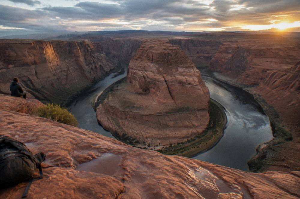 Wide desert horizon above a river bend with layered orange rock walls under evening sky.