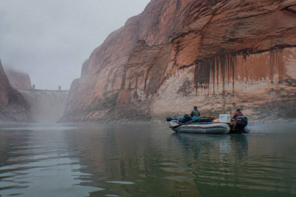 A motorized raft drifting on flat green water beneath tall rock cliffs.