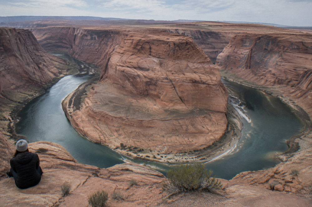 A wide desert river bend curving between layered orange sandstone walls.