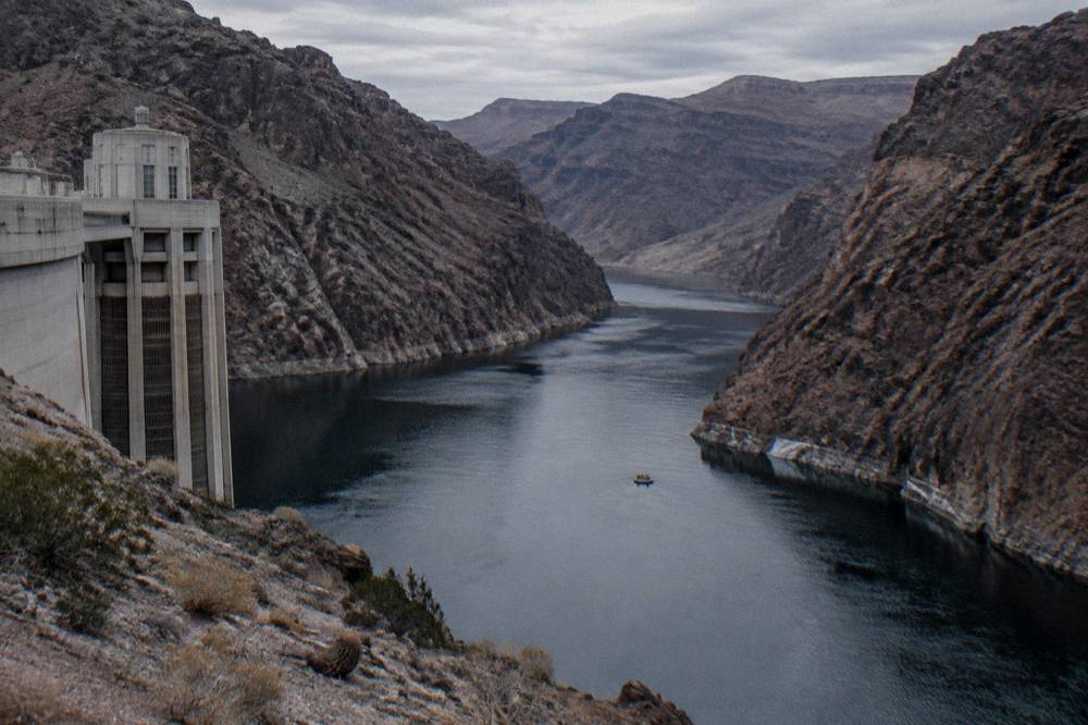 Steep dark rock walls rising above calm river water with a small raft in the distance.