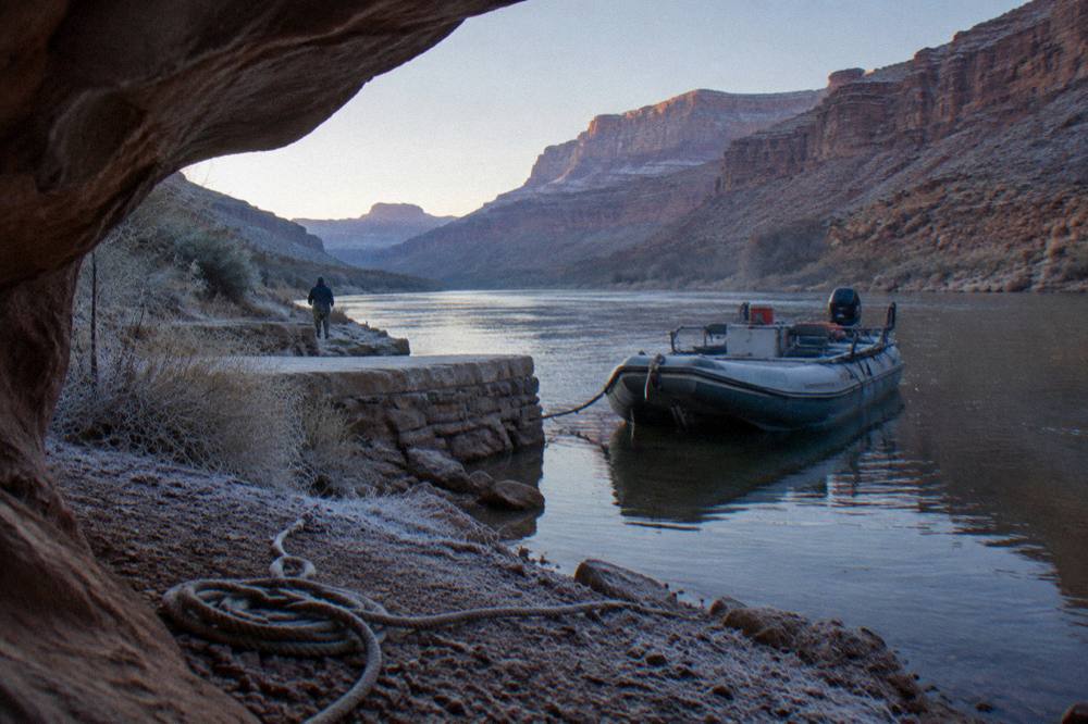 A raft loading area at a river launch beside calm water and rocky desert shoreline.