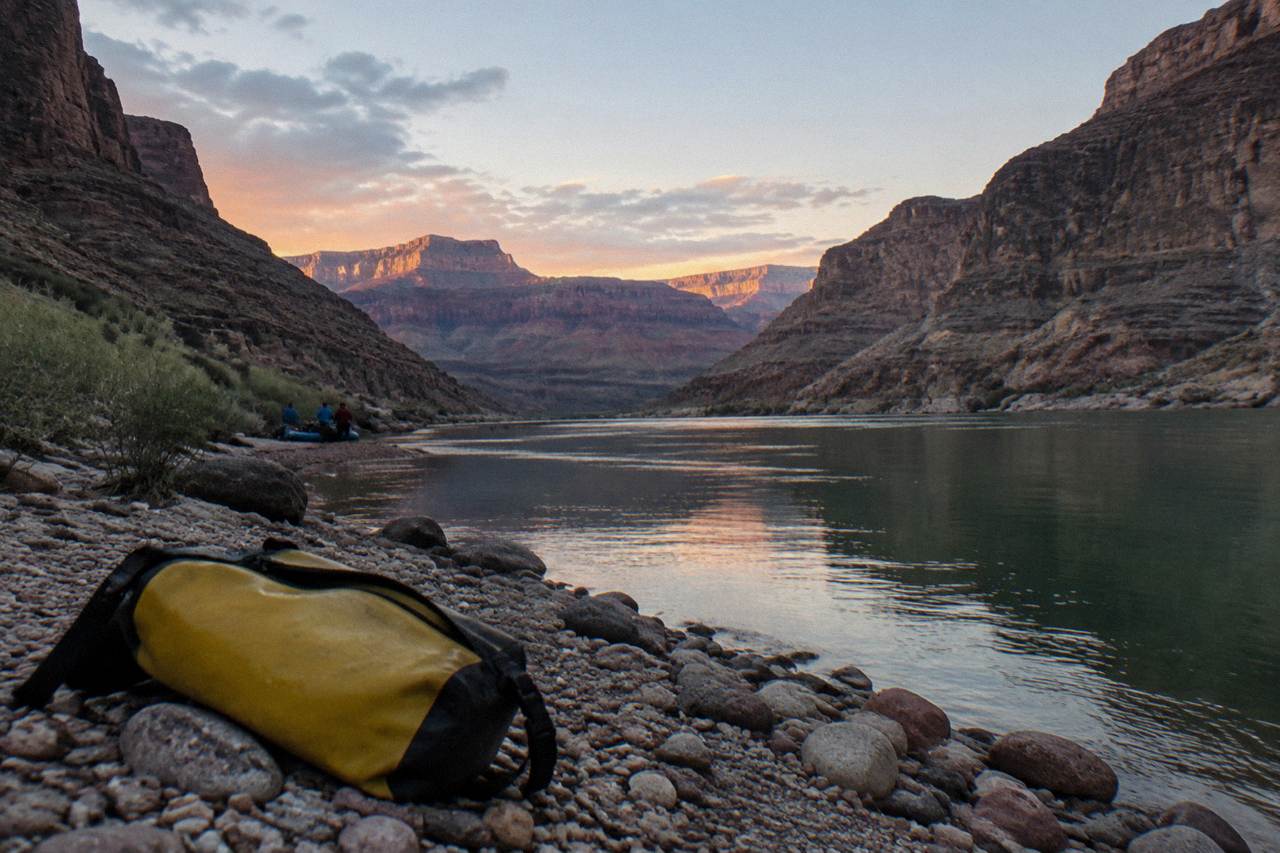 A calm stretch of the Colorado River winding between dark canyon walls under a wide sky.