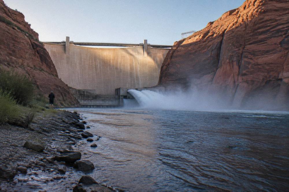 Concrete dam wall releasing water into a river channel below