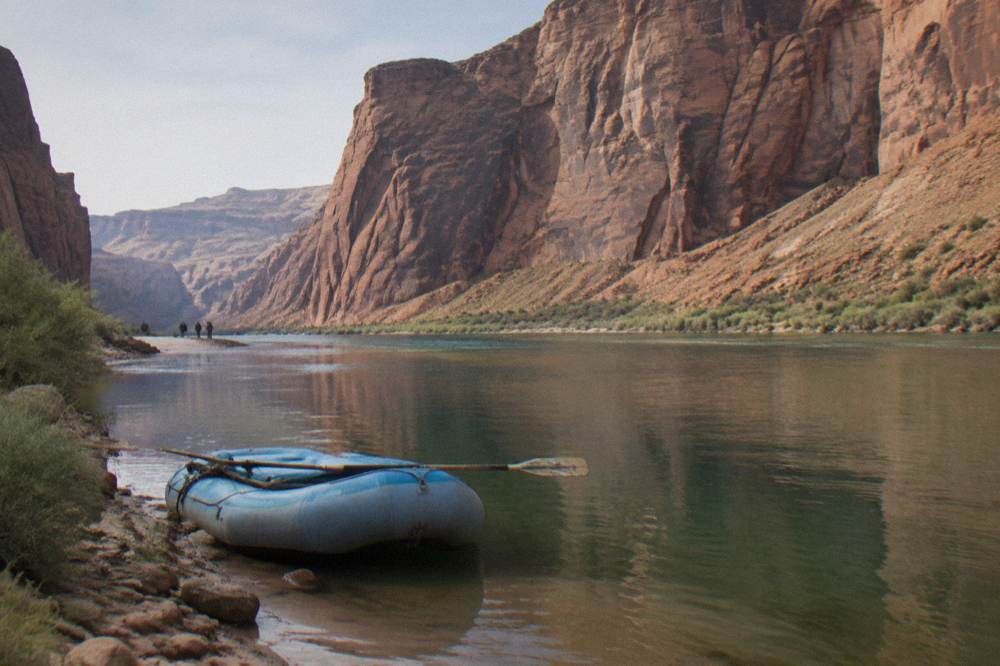 Raft floating on calm water beneath tall sandstone cliffs at Horseshoe Bend
