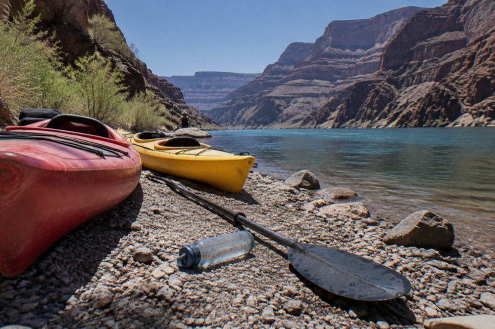 Two kayaks resting on a rocky beach beside a narrow river canyon at midday