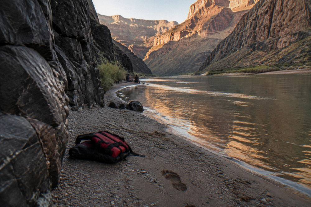 A calm river beach inside a narrow canyon with warm evening light on the rock walls