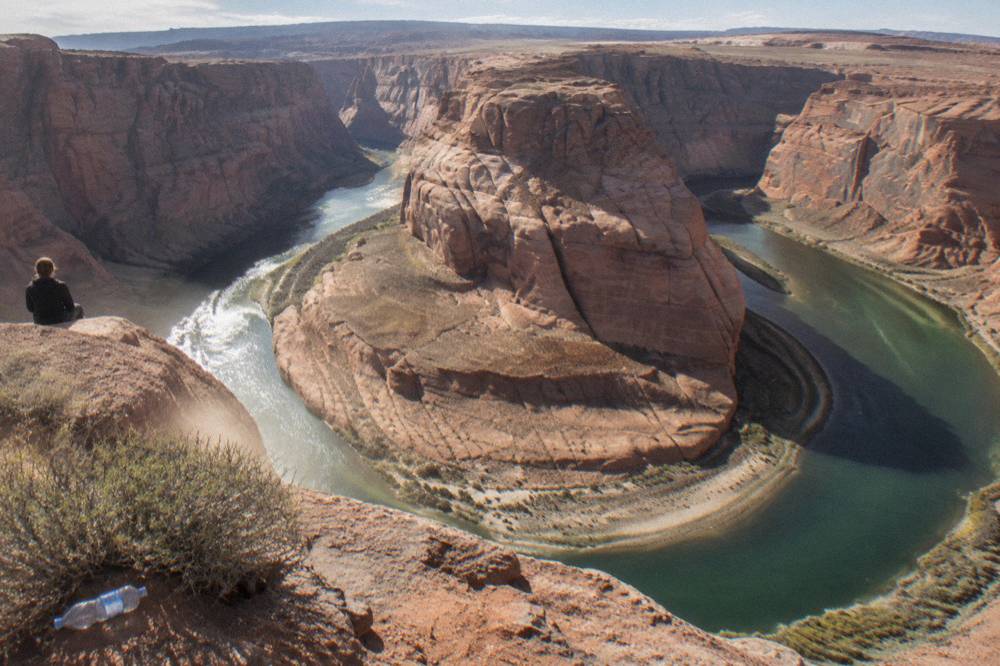 Sweeping aerial-style view of a river bend curving around a tall sandstone butte under open sky