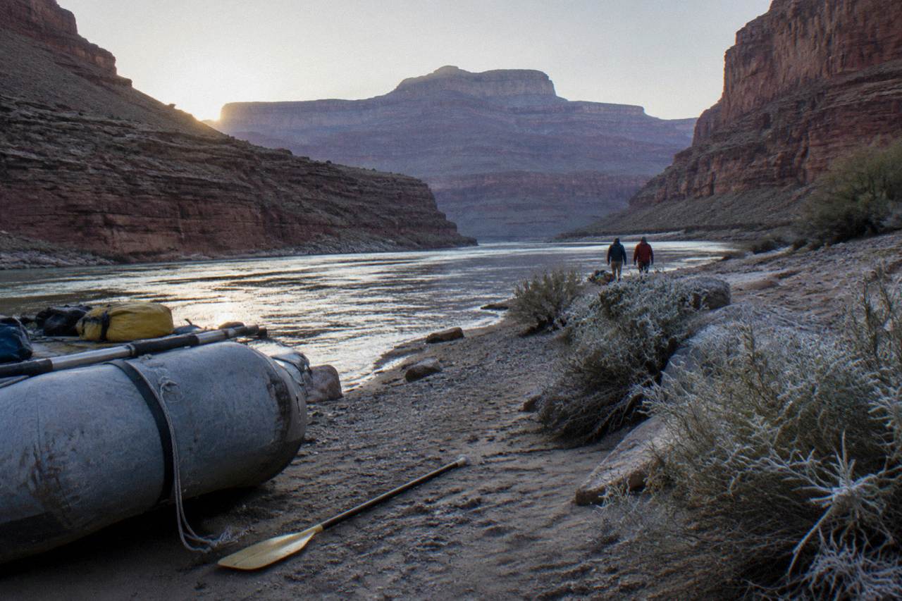 Wide desert view of the Colorado River winding below tall canyon walls at dawn