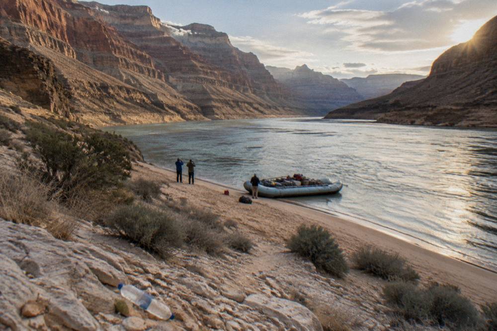 A motor raft pulled onto a sandbar while guests take photographs of the canyon walls