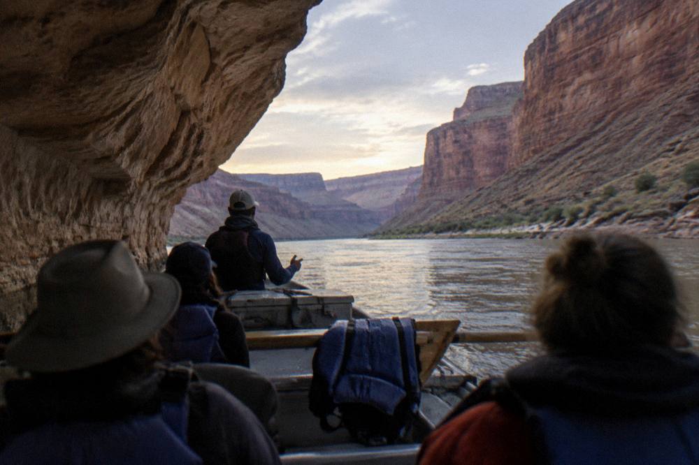 Guests seated on a motor raft listening to a guide in a narrow canyon passage