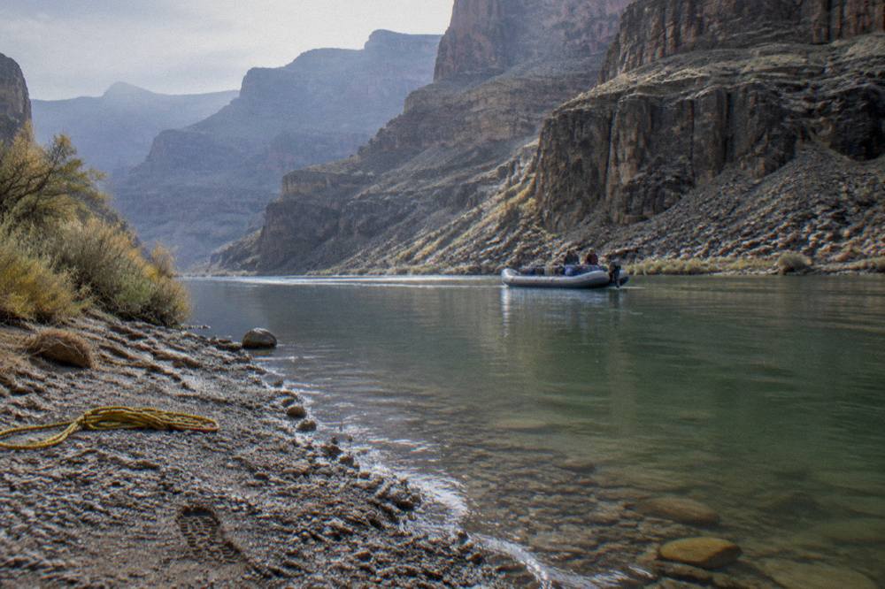 A motorized raft drifting along calm green water beneath tall volcanic canyon walls
