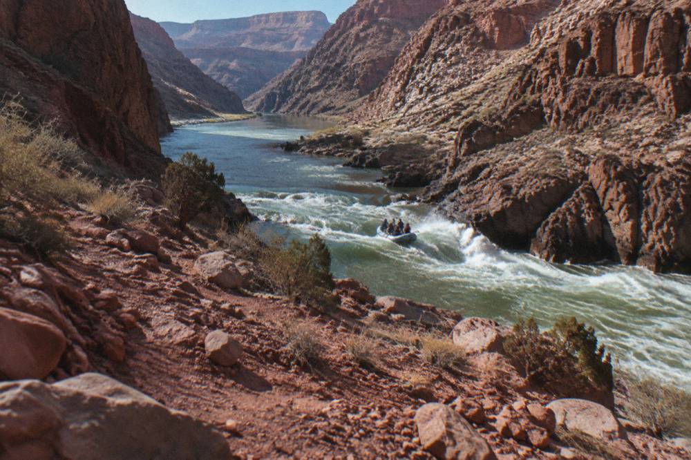 A whitewater raft cutting through a rapid between steep red canyon walls