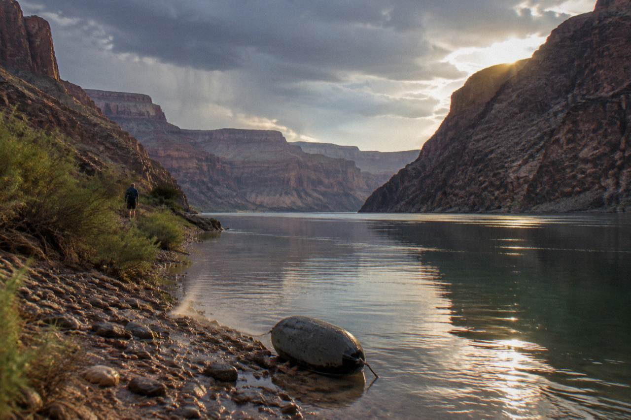 A calm stretch of the Colorado River winding between dark canyon walls under a wide sky
