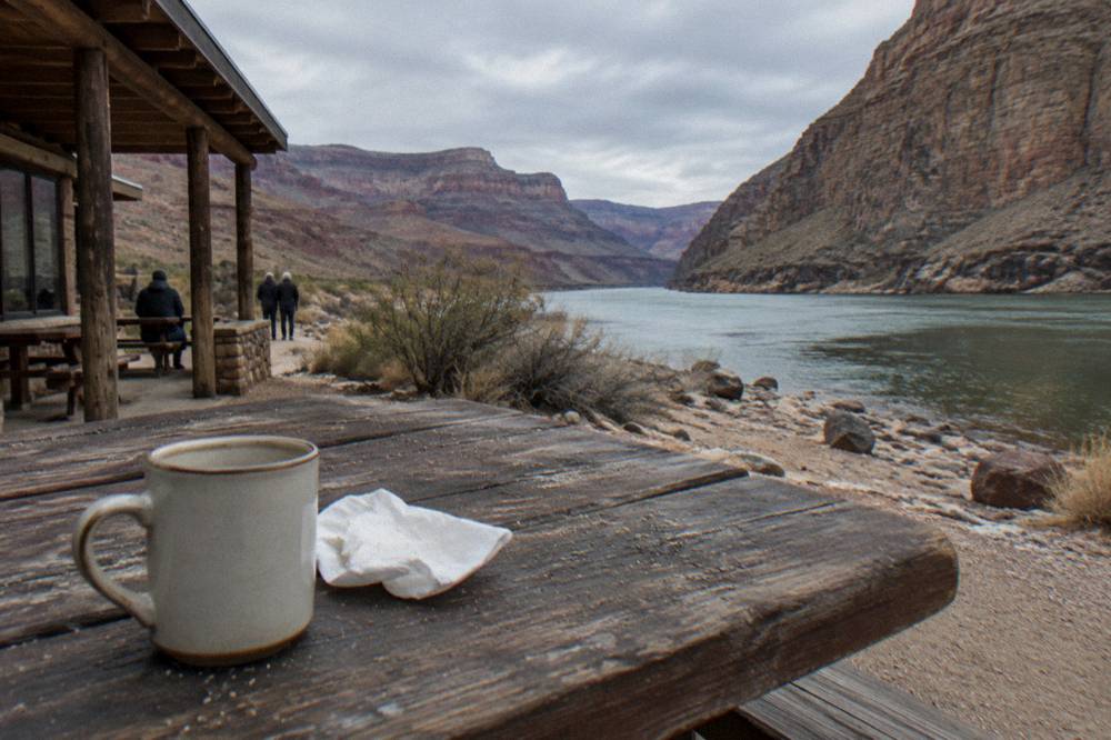 A picnic table set with food beside a river beach between canyon walls