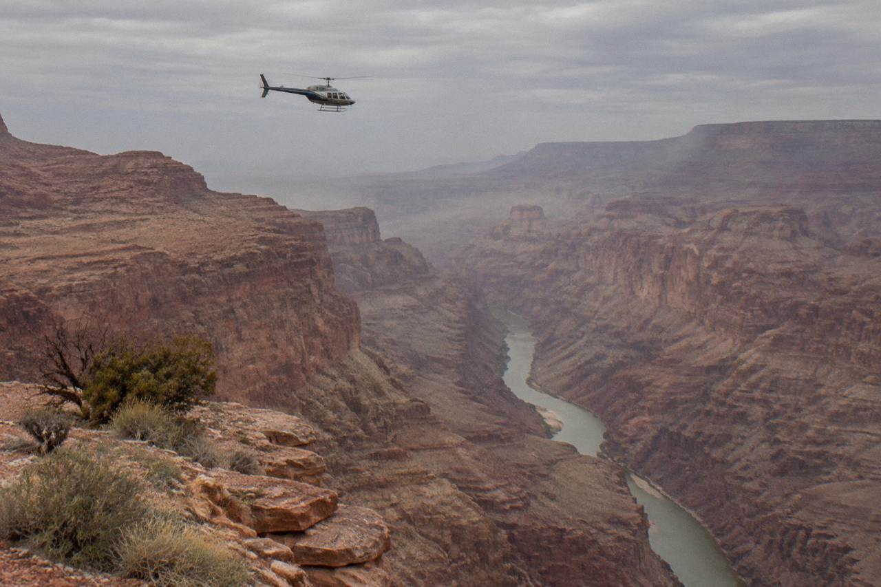 A helicopter flying above a narrow desert canyon with the Colorado River below