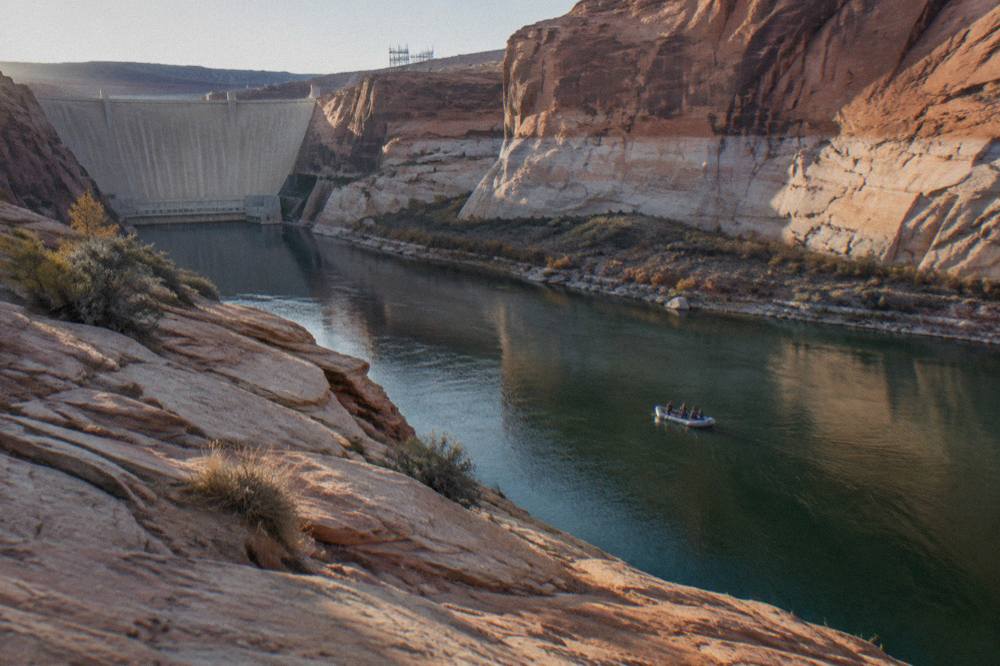 A motorized raft carrying passengers down a calm stretch of the Colorado River between canyon walls