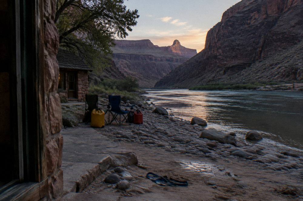 Camp chairs and dry bags arranged on a river beach at dusk with canyon walls rising behind
