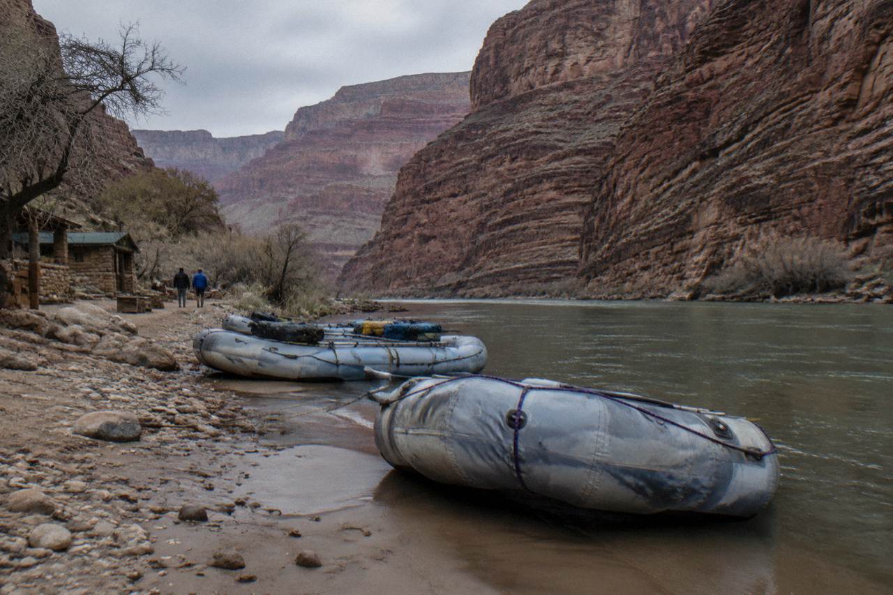 Rafts moored on a sandy Colorado River beach inside a tall red rock canyon