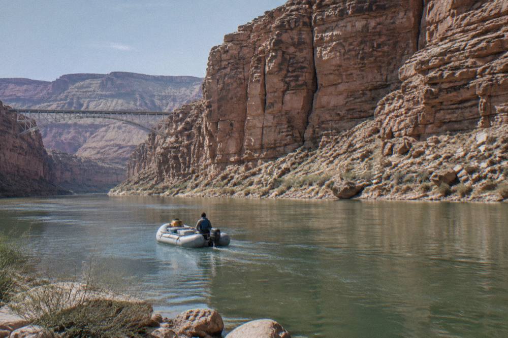 A motorized raft drifting on calm green water beneath tall red canyon walls