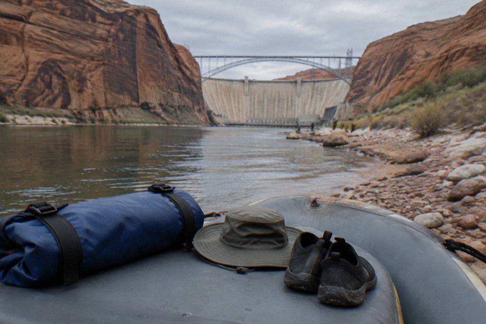 A dry bag, sun hat and water shoes arranged on a raft seat beside a river