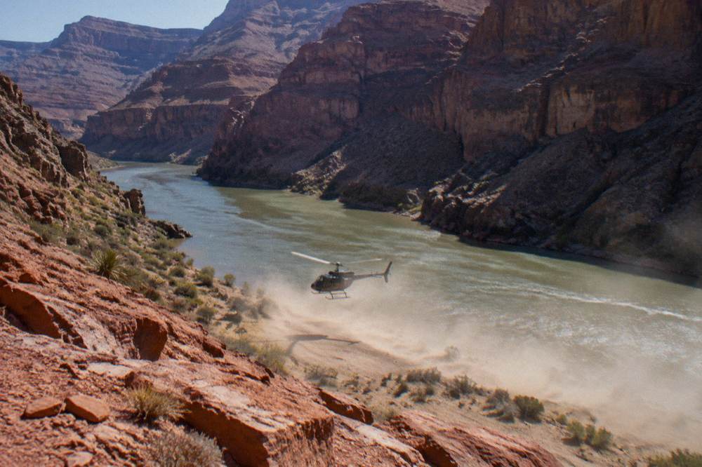 A helicopter lifting off from a riverbank inside a deep canyon