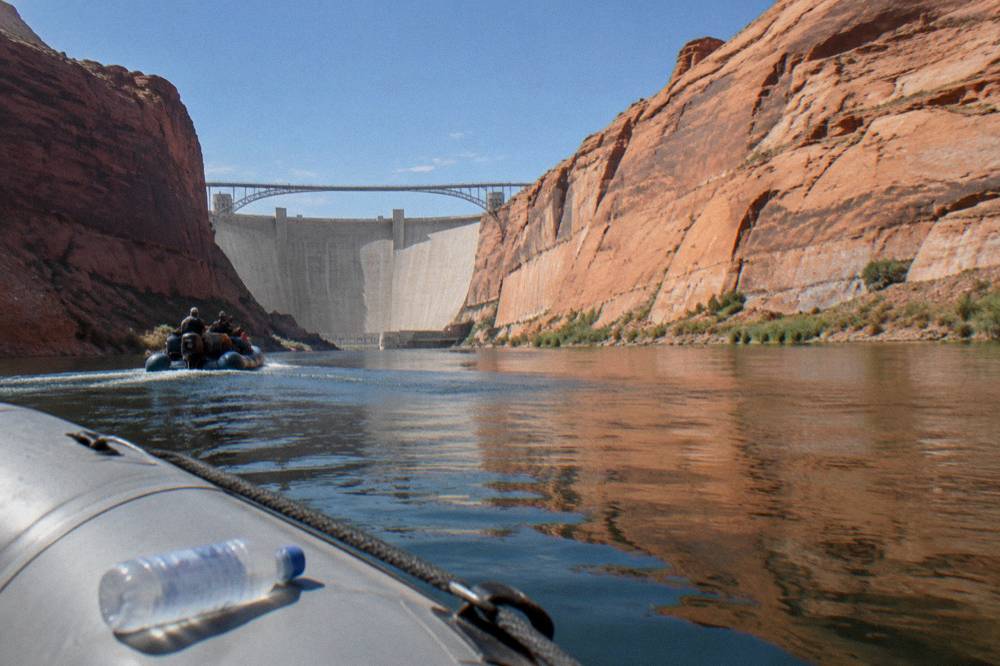 A motor raft carrying passengers along a glassy river bend beneath orange sandstone cliffs