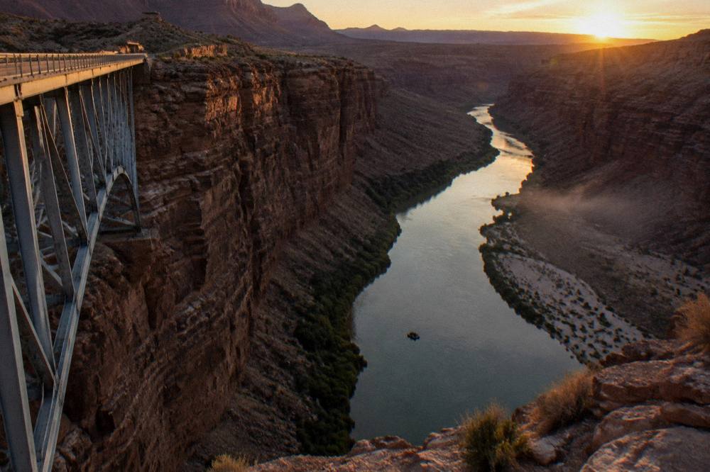 A calm river corridor at sunset with a raft silhouette far downstream between dark canyon walls