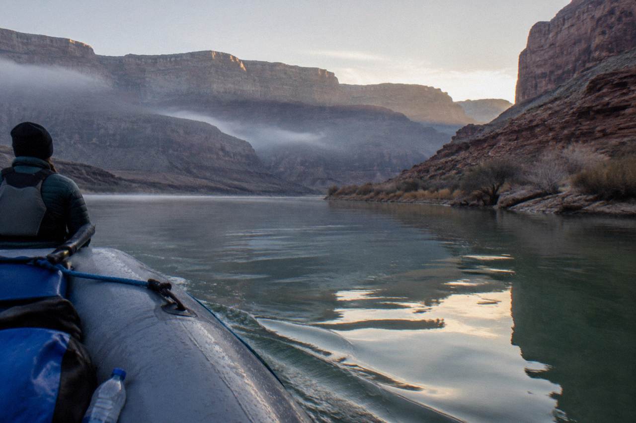 A motorized raft drifting on the calm Colorado River between tall canyon walls at dawn