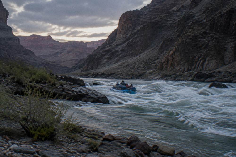 A raft cutting through foamy whitewater between dark narrow canyon walls