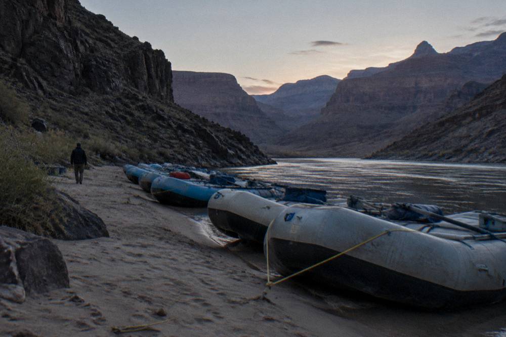 A row of inflated rafts moored on a sandy river beach at dusk