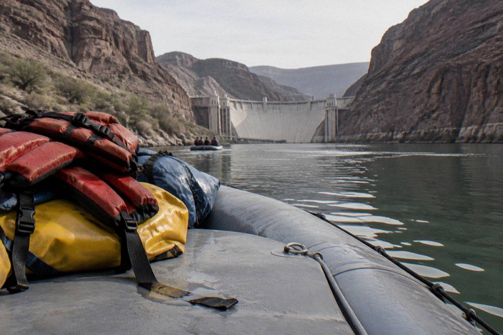 Life vests and dry bags stacked on a raft deck beside calm river water