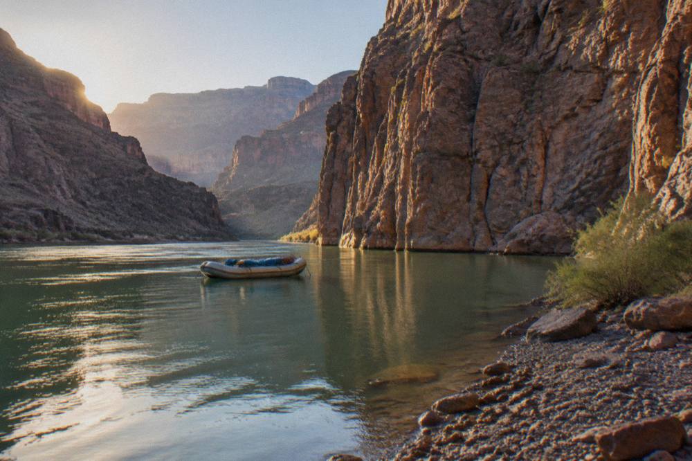 Raft floating on still green water beneath tall volcanic canyon walls