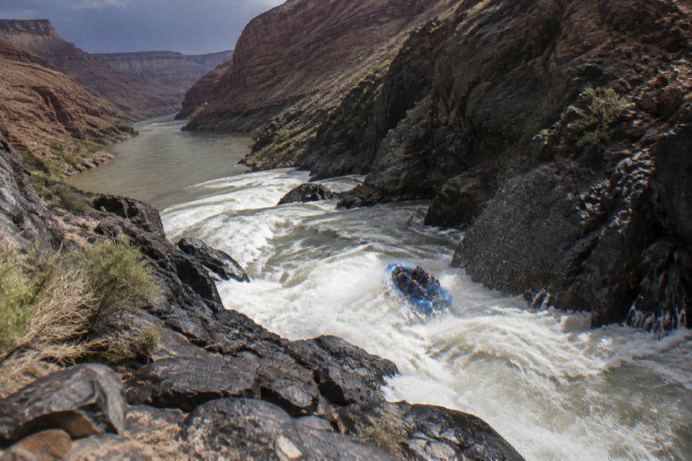 Whitewater raft cutting through a rapid between steep canyon walls