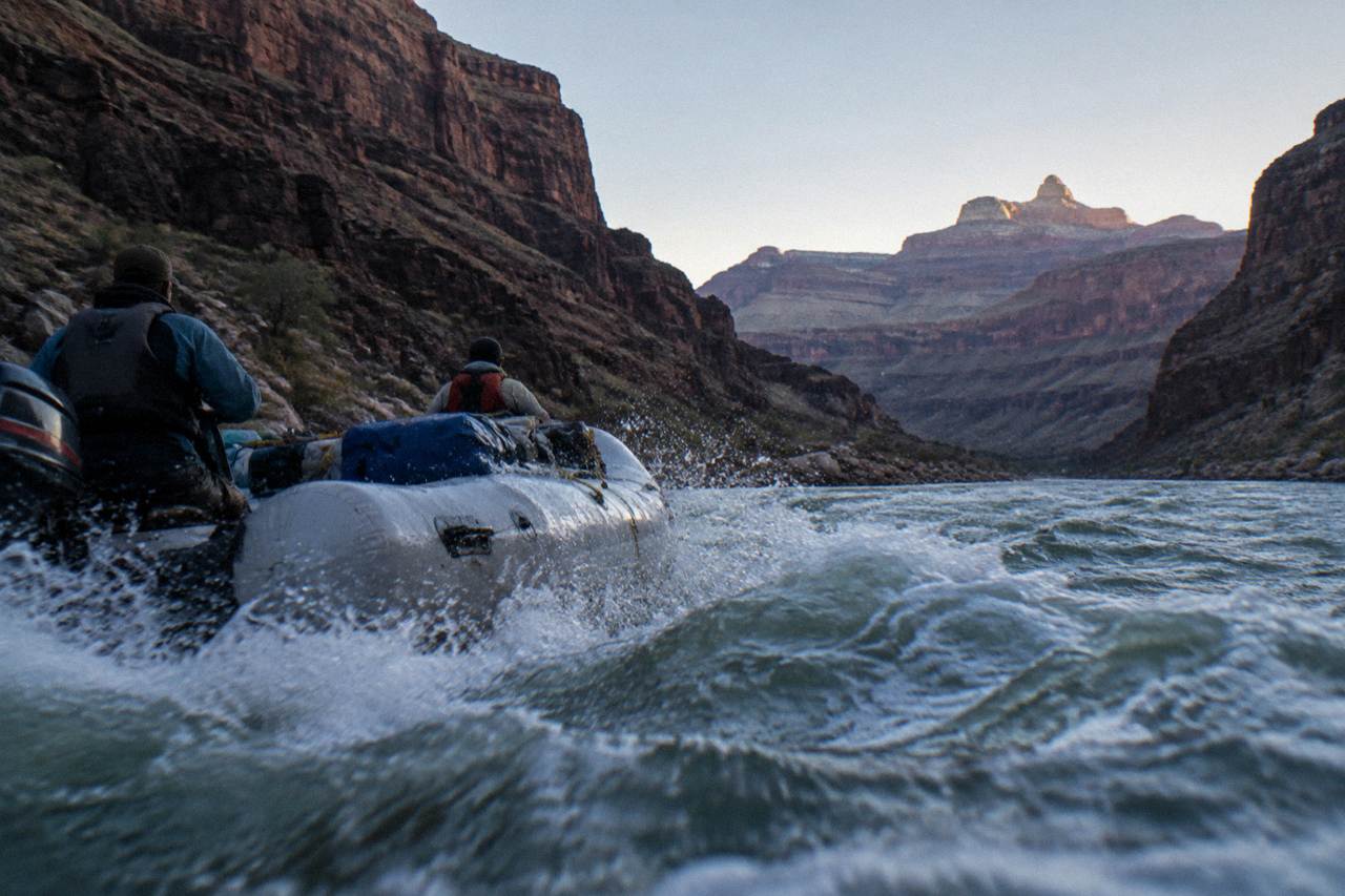 A motorized raft running a rapid between dark canyon walls on the Colorado River