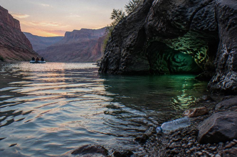 A small cave opening at water level reflecting green light onto the river surface