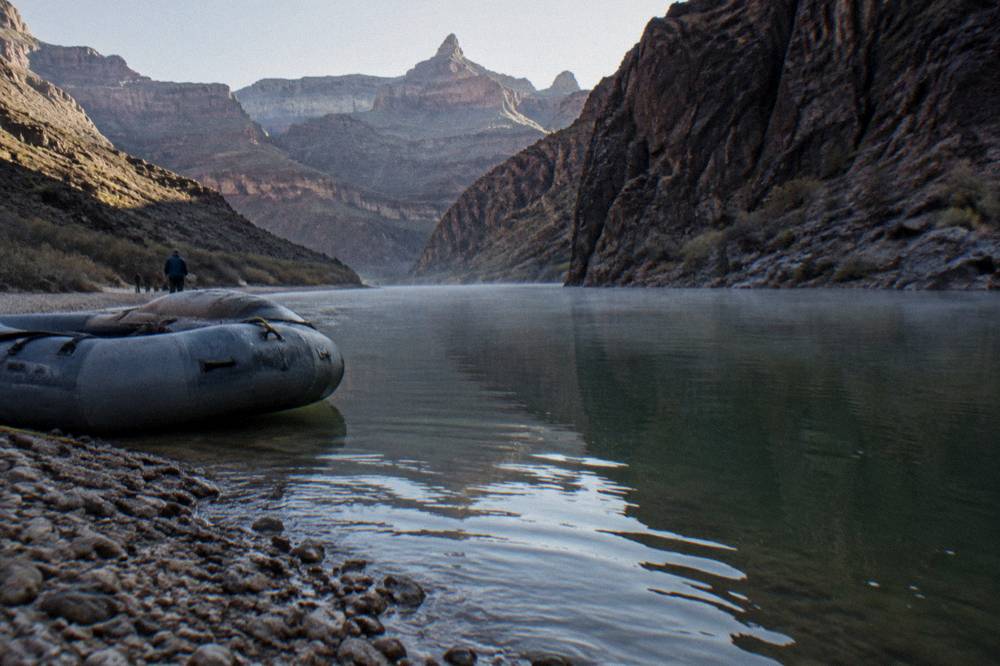 Morning light on a glassy river channel between steep dark canyon walls