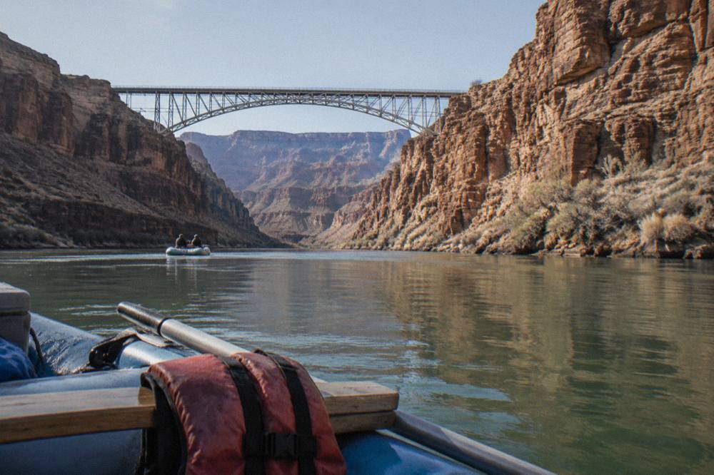 A motor raft drifting on flat green water between tall sandstone walls on the Colorado River