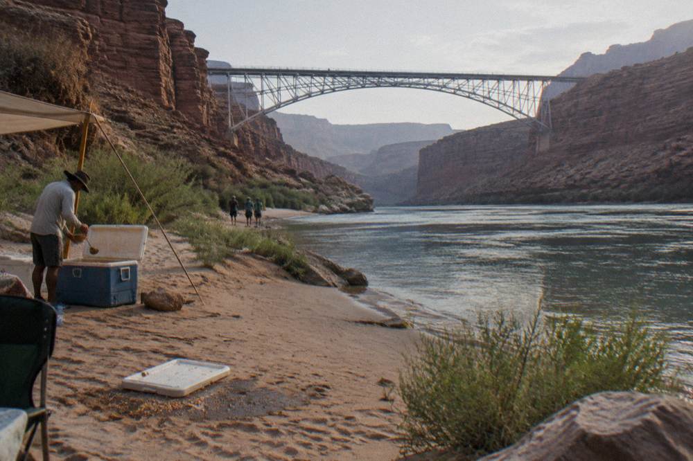 A guide serving lunch to raft passengers on a sandy beach along the Colorado River