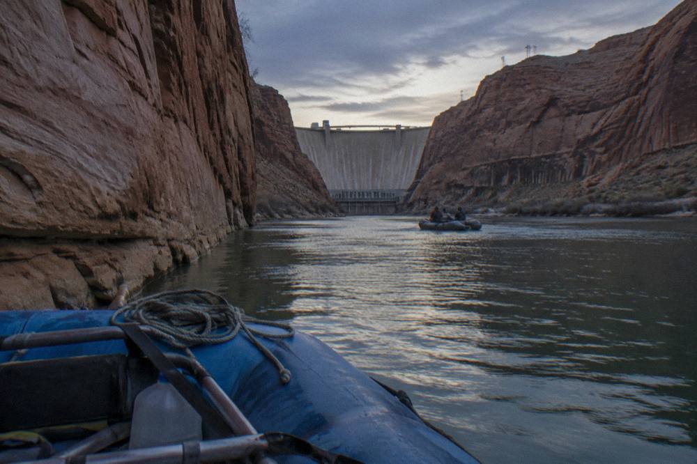 A raft floating past tall rock cliffs above a still green river