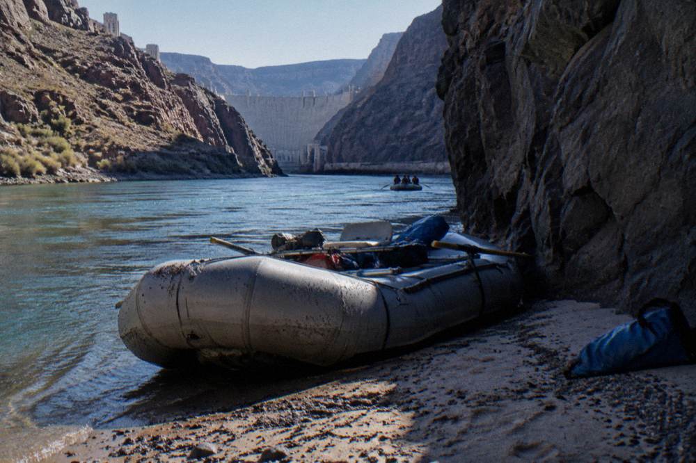 A tour raft pulled up on a sandy beach beside a narrow river bend