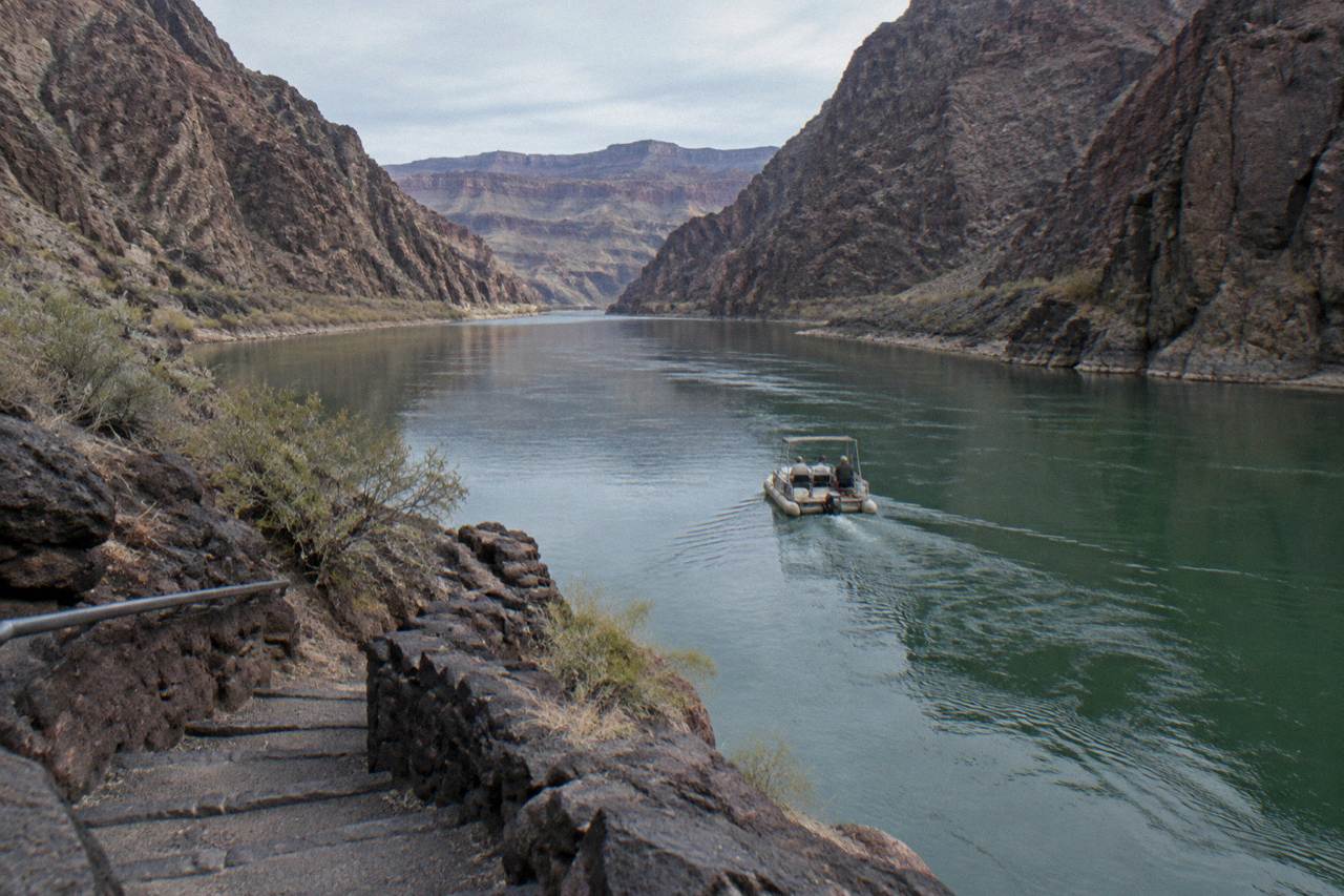 A motorized raft drifting on calm green water between dark canyon walls