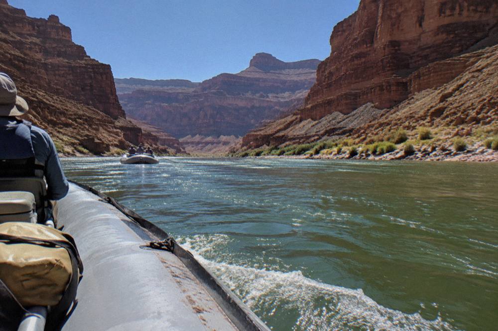 A motorized raft on the green water of the Colorado River between steep canyon walls