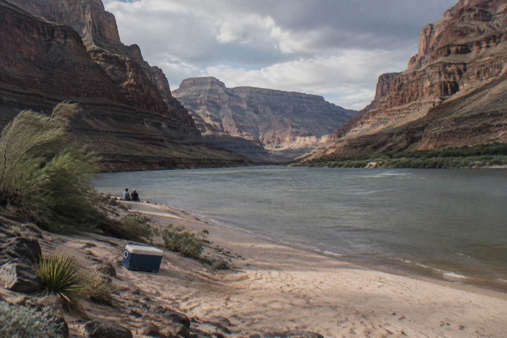 A sandy beach along the Colorado River at the base of high canyon cliffs