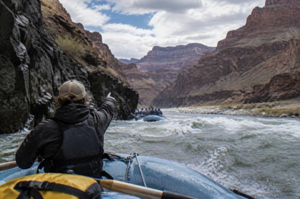 A raft guide pointing out canyon features to passengers on the river