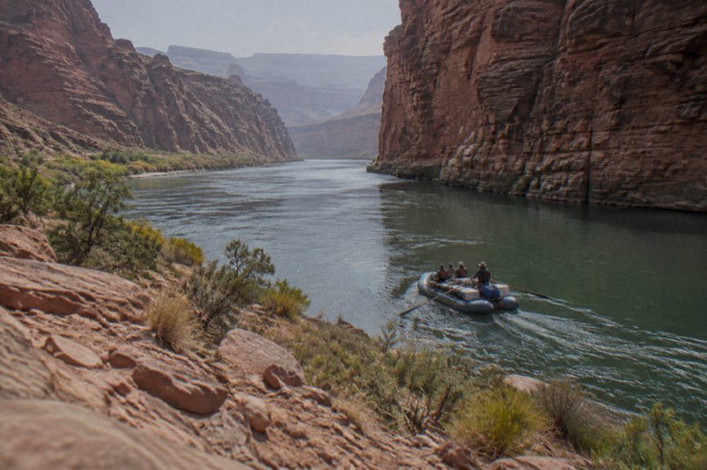 A guided motor raft passing between tall red rock canyon walls on the Colorado River