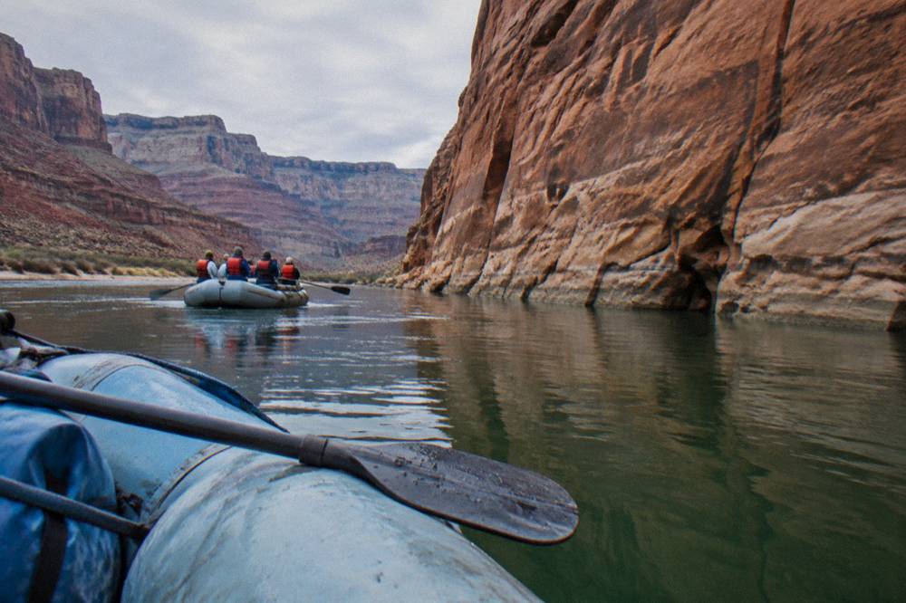 A family seated in a raft on calm water wearing life jackets near a canyon wall
