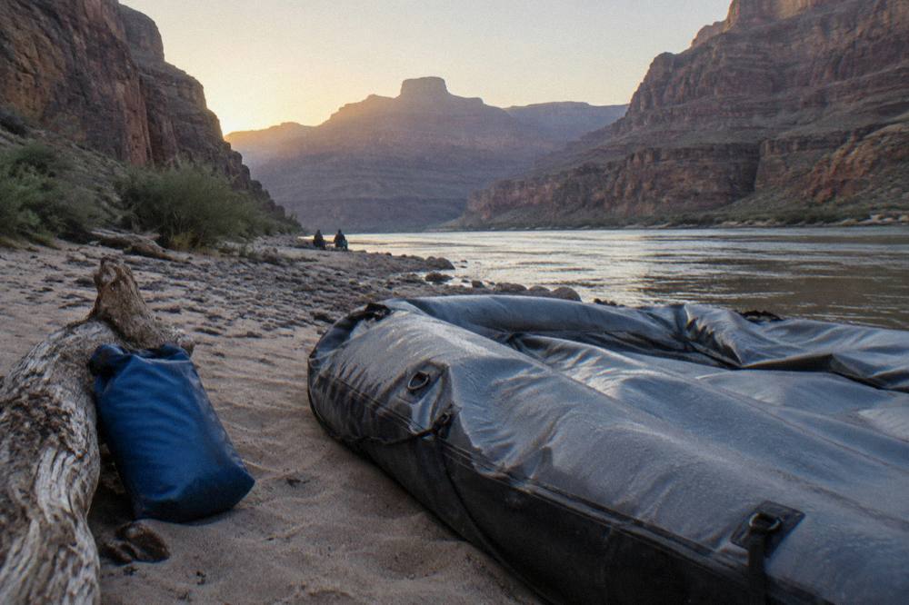 A raft resting on a sandy beach beside the river inside a deep canyon